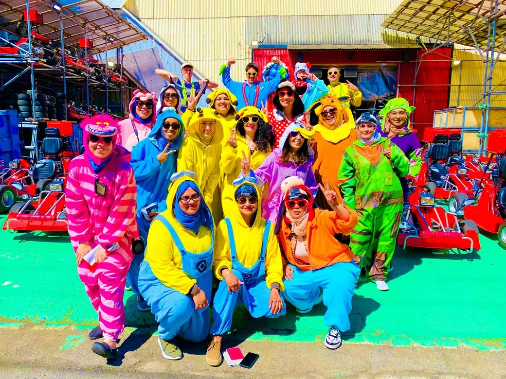Group of people in bright Minion costumes posing for a photo at a go-kart track area.